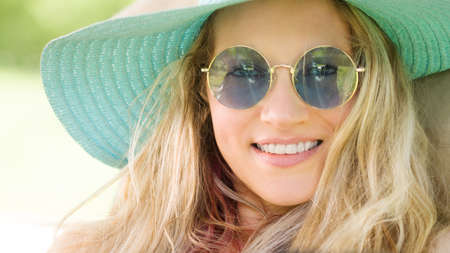 Smiling blonde woman wearing sunglasses and blue straw hat, laughing portrait, leisure and summer...
