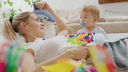 Happy smiling mom plays with her beautiful baby, with colorful educational learning toy, sitting at...