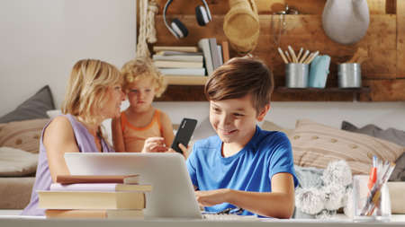 happy family at home, mother with daughter and son have fun using computer and mobile phone, surf the internet, comfortably in living room using technology devices, social media and modern lifestyleの写真素材