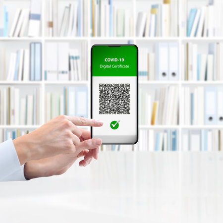 Green pass covid-19 vaccination concept. Hands holds smartphone with qr code digital vaccine certificate on screen. isolated on library background.の写真素材