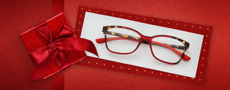 glasses merry christmas gift card, red package box with shiny ribbon bow, red spetacles isolated on white ticket, top view, layout useful as gift or pricing card or greeting cardの写真素材