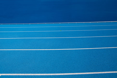Blue Olympic track lanes with white stripes, an empty background suitable for copy space, represent the concept of physical sports and running, symbolizing commitment and pathways towards goalsの写真素材