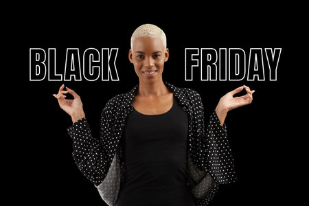 Black Friday shopping. Smiling African woman pointing at a text written isolated on black background. Banner commercial sign. Store and mall advertising Billboard guiding shoppersの写真素材