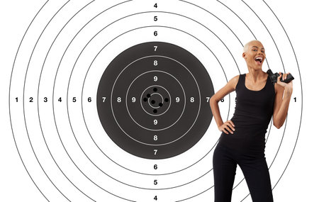 Hit the target, concept of achieving set goals. African smiling woman with gun isolated on white background with shooting target. Banner advertising commercial sign.の写真素材