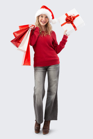 Happy merry Christmas woman wearing Santa hat holds gift box and red shopping bags. Image for sale offer promotions, online shopping, advertising banner, poster, or gift card, isolated backgroundの写真素材