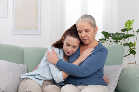 Caring elderly grandmother hugs and comforts her upset granddaughter at home. Emotional and touching...