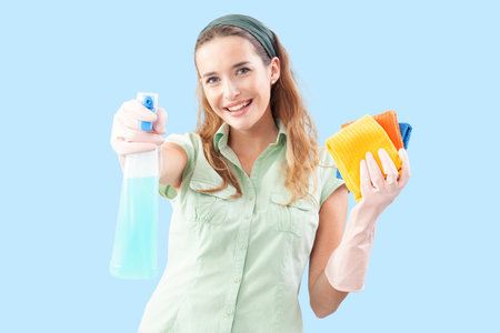 Smiling woman holding a spray bottle and cleaning cloths and looking at the camera. Front view,...