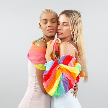 Emotional and loving hug between an LGBTQ lesbian couple, isolated on white background, wearing rainbow pride themed clothing. Concept of love, diversity, inclusion, and equal rightsの写真素材