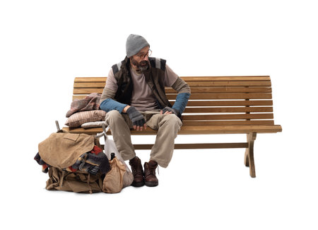 A homeless man sitting on a wooden bench isolated on white, illustrating poverty, hunger, urban hardship, and survival.の写真素材