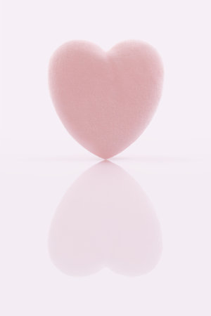A single soft pink heart shaped makeup puff, suitable for applying powder, foundation, or removing makeup. The beauty product is isolated on a glossy reflective surface. Skincare conceptの写真素材