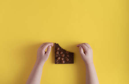 Children's hands keep the chocolate on a yellow backgroundの写真素材