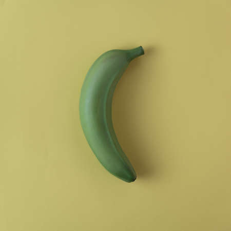 Green banana isolated on yellow background. Creative minimal summer ideaの写真素材