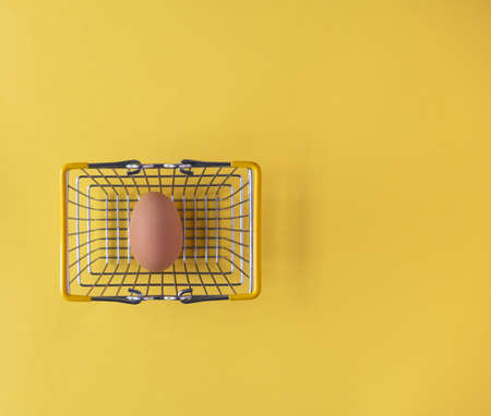 Easter egg in a basket on a yellow background with creative copy space. Minimal Easter holiday conceptの写真素材
