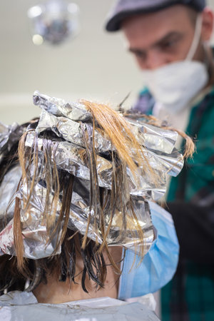 woman being combed by hairdresser with spray and blow dryer in front of mirror in modern retro hair salonの写真素材