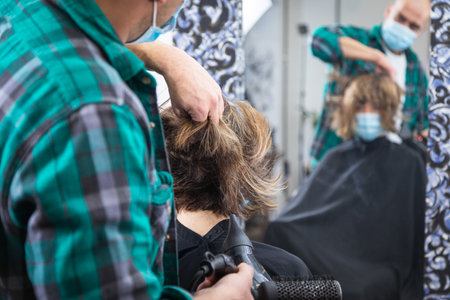 woman being combed by hairdresser with spray and blow dryer in front of mirror in modern retro hair salonの写真素材