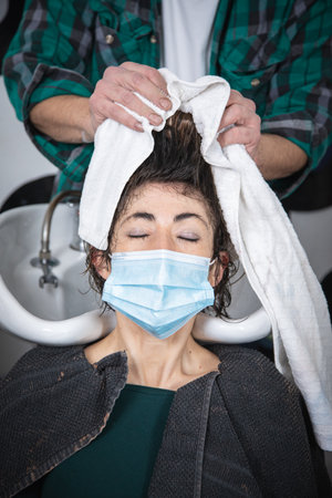 woman being combed by hairdresser with spray and blow dryer in front of mirror in modern retro hair salonの写真素材