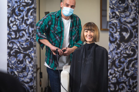 woman being combed by hairdresser with spray and blow dryer in front of mirror in modern retro hair salonの写真素材