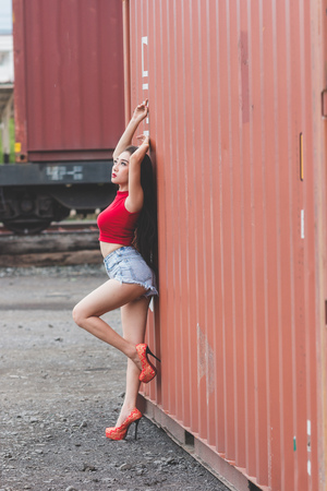 Portrait of fashion pretty hot girl wearing a red shirt at outdoors,Containers are the background.の写真素材