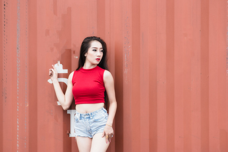 Portrait of fashion pretty hot girl wearing a red shirt at outdoors,Containers are the background.の写真素材