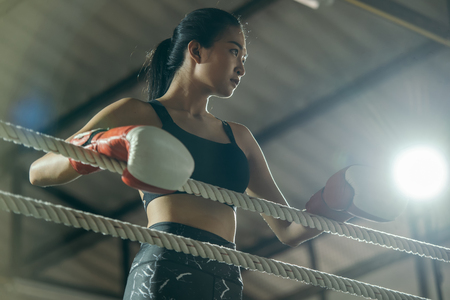 Upset young fighter boxer girl wearing boxing gloves in gymà¸¡Female boxer taking a break from her practice.の写真素材