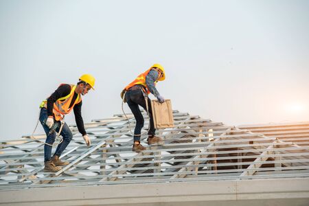 Construction worker wearing safety harness belt during working on roof structure of building on...