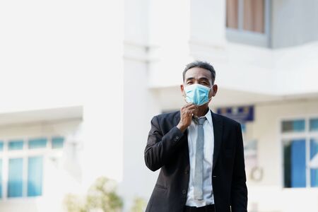 Businessman wearing medical mask for coronavirus covid 19 protection standing beside office building in city,Coronavirus Disease 2019 (COVID-19),Coronavirus has turned into a global emergency.の写真素材