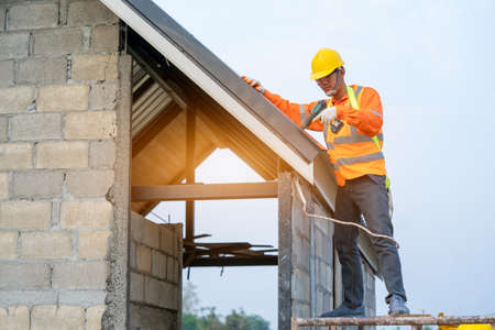 Roofer working on roof structure of building on construction site,Worker installing metal roof on...
