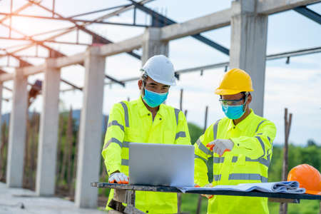 Two engineers wearing protective mask to Protect Against Covid-19 and checking production process in building construction site,Construction,Building, teamwork and people concept.の写真素材