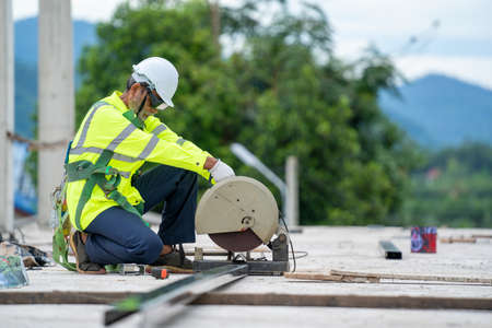 Industrial construction engineer cutting steel using angle miter saw at building site.