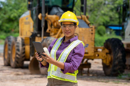 Engineer women use tablet for working at construction site.Real Estate Building Project with construction car vehicle at the work area.の写真素材