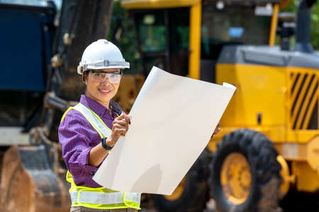Female engineer worker on construction site outdoors with excavator in background,construction Site,construction machinery, bulldozer, excavation.の写真素材
