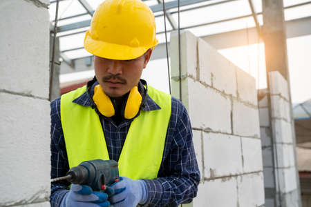Construction workers using a drilling power tool for drilling aerated bricks on construction site.