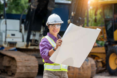 Engineer or architect women holding blueprints with loader truck at construction site,Engineering construction car vehicle at the work area.の写真素材