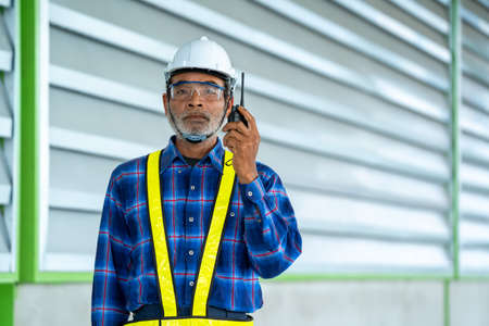Engineer using walkie-talkie while colleagues discussing in warehouse.の写真素材