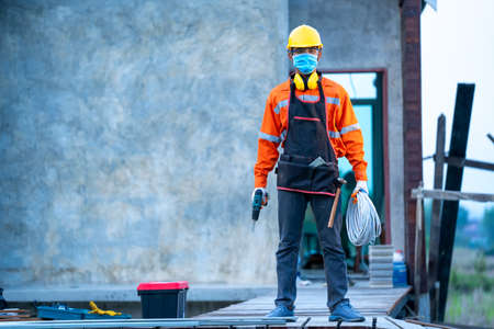 Electrician wearing protective mask to Protect Against Covid-19 with bunch of wires indoors at construction site.の写真素材