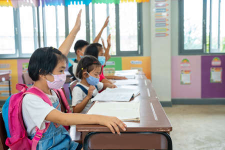 Group of school kids wear protective masks with teacher sitting in classroom and raising hands,learning and people concept.の写真素材