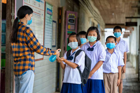 Teacher and elementary children with face mask are disinfecting hands at school after covid-19...