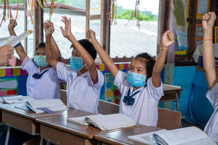 Asian children student wear face mask learning in classroom at elementary school,Student raising their hands to answer questions that teachers ask them,Asian Student Education Concept.の写真素材