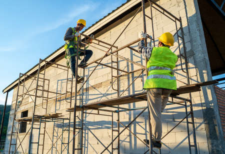 Construction workers in uniform and safety equipment working on scaffolding at building site.の写真素材