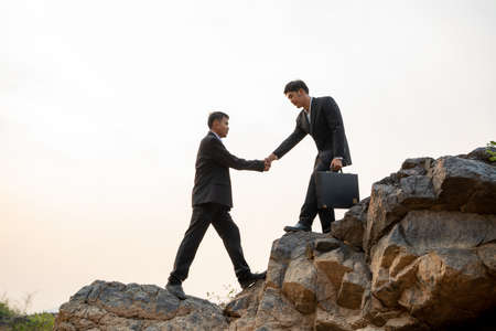 Businessman helping each other hike up a mountain at sunset background,Business teamwork success concept.の写真素材