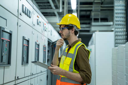 Engineer working on works on a tablet computer in switchgear room of a modern thermal power plant at...