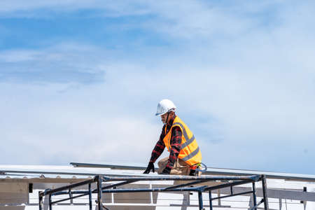 Roofer worker in protective uniform wear and gloves working installing metal sheet on top of the new roof at construction site.の写真素材