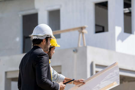 Architects discuss with head engineer about construction project on workplace at construction site.