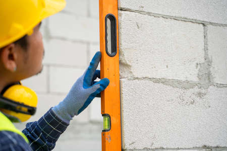 Engineer measures the work out wall lightweight concrete blocks with a level at construction site.の写真素材