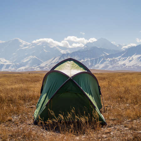 Wild camping tent set in the middle of the valley surrounded by beautiful mountains covered with snow in Kyrgyzstan Pamir mountainsの写真素材