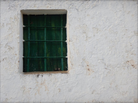 Old wooden window with green bars on an old white facadeの写真素材