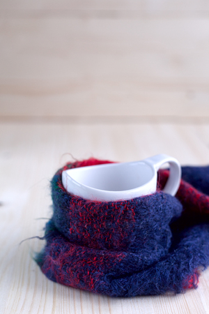 White Cup with tea standing on wooden planks, tied with a scarf of dark colorの写真素材