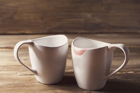 Two white cups, one of them is wearing lipstick, the relationship of men and women, Valentine's day, on the background of old wooden planksの写真素材