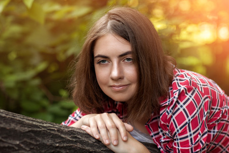 A young girl is sitting outdoors on the grass in a tree, brooding look, a summer day outdoors in the Park.の写真素材