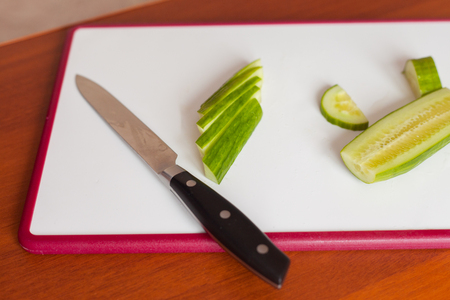 On the white Board is a knife and sliced cucumber.の写真素材